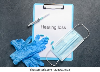 Clipboard With Text HEARING LOSS, Medical Mask, Gloves And Pills On Dark Background