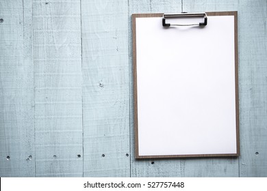 Clipboard with white sheet on wood background. Top view. Mock up for word.