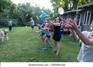 CLITHERALL, MINNESOTA / USA - JULY 14, 2017: Extended Family Of Three Generations And A Dog Playing Water Balloon Toss. 