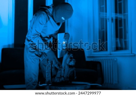 A cloaked figure organizes tools, preparing for a break-in, with a sinister lamp illumination suggesting an upcoming crime