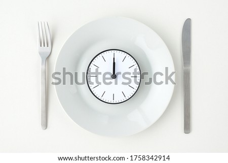 Clock with 12 o'clock on white plate with fork and knife