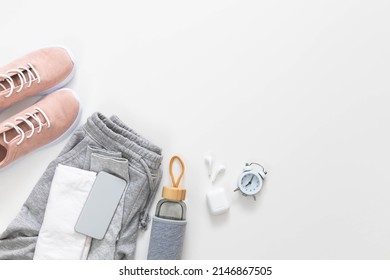 Clock alarm and devices for morning jogging. Top view beige sneakers, reusable glass water bottle, bra, pants, smartphone and earphones isolated with copy space. Concept of physical jerks and training