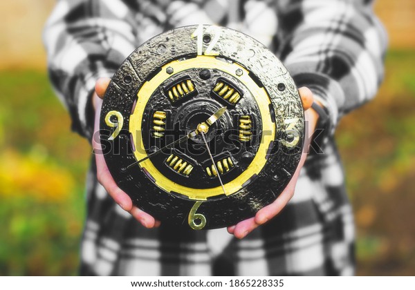 A clock from a car clutch\
disc. Black watch with gold elements. Man holding a clock in his\
hands