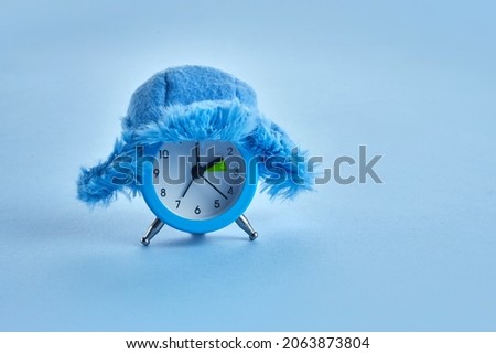Clock changing from summer to winter time. Alarm clock with winter hat