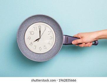 Clock face in a frying pan showing 8 a.m. on blue background. food Time. Time to eat concept. Breakfast time. frying pan in woman's hand on blue background. Woman holding a pan in a hand. Diet concept