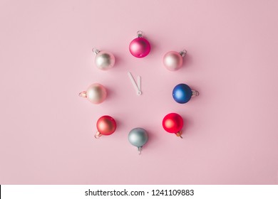 Clock hands with colorful pastel decoration balls on pink painted wall. Minimal time concept. Chrismas eve or new year idea.