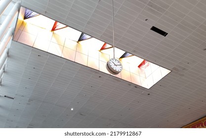 a clock hanging from the ceiling of a building with a window perched on the ceiling