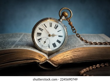 The clock lies on an old book. Clock as a symbol of time, the book is a symbol of knowledge, science.  Concept on the topic of history, science, memory, information. Vintage watch, clock background.