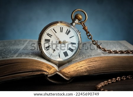 The clock lies on an old book. Clock as a symbol of time, the book is a symbol of knowledge, science.  Concept on the topic of history, science, memory, information. Vintage watch, clock background.
