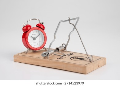 Clock and mouse trap set on a table before a white background in a simple display showing the concept of time and traps