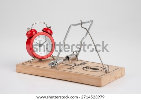 Clock and mouse trap set on a table before a white background in a simple display showing the concept of time and traps