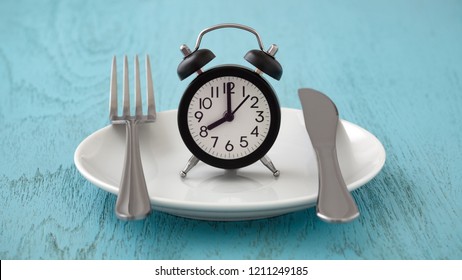 Clock on white plate with fork and knife, intermittent fasting, meal plan, weight loss concept on blue table - Shutterstock ID 1211249185