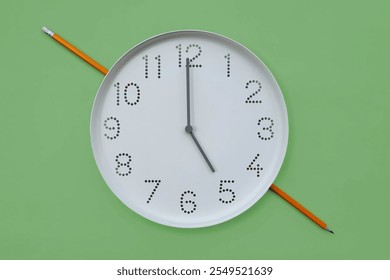 Clock and pencil. Round white wall clock shows 5 o'clock on plain green background copy space. Symbol of working hours, end of work in office or study at 17 oclock, deadline - Powered by Shutterstock