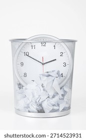 Clock placed inside a wire trash bin filled with crumpled paper at a work desk