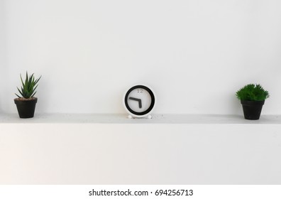 Clock with pots at white wall 