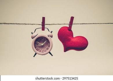 A clock and a red heart hung together on a rope / time and love concept