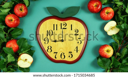 Clock in the shape of an apple creative concept flatlay with fresh apples on green background.