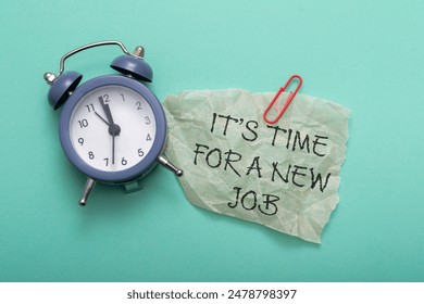 A clock sits on a table next to a piece of paper that reads, It's time for a new job, signaling a moment for change.