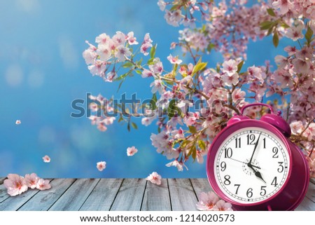 Clock and spring cherry flowers on wooden table - daylight saving time concept