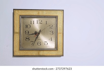 The clock is square in shape. It features a decorative outer frame consisting of four golden, textured panels that have a 
