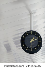 A clock is suspended from the ceiling in a train station platform showing the time to passengers below