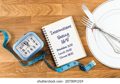 Clock, Tape Measure, Dish With Cutlery And Notebook With A 168 Intermittent Fasting Meal Schedule. Concept Of Intermittent Fasting, Diet With Benefits Such As The Regeneration Mechanism Of Autophagy.