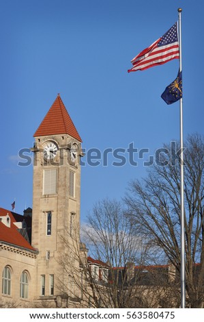 The clock tower with flags in front of it on a clear day with a blue sky at Indiana University in Bloomington, Indiana.
