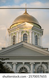 A clock tower in front of a building. High quality photo, dome of the orthodox church. golden color, the building is painted blue. the sky is a soft blue color with clouds