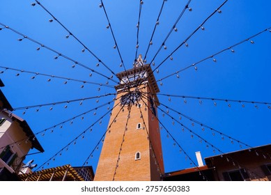 Clock tower with hanging string lights radiating outward under clear blue sky in urban setting