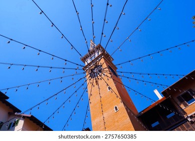 Clock tower with hanging string lights radiating outward under clear blue sky in urban setting