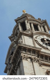 A Clock tower with multiple clocks with a golden statue on top, viewed from below
