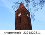 Clock tower in the old town. Clock in Poland, Lubin. European architecture of the past. The clock tower on the background of the blue sky behind the tree branches