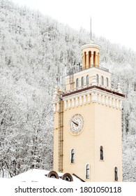 The clock tower on the background of the mountain with snow-covered trees