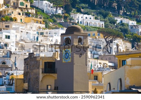 Clock tower in Piazza Umberto, knows as La Piazzetta, Capri, Italy, stands against backdrop of Mediterranean-style buildings with white and pastel facades