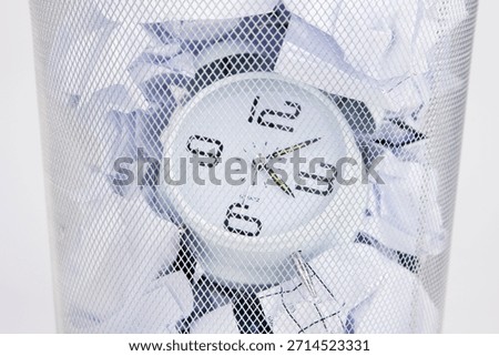 Clock trapped in a waste bin surrounded by crumpled paper on an ordinary day in an office setting