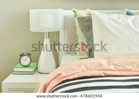 Clock and white table lamp next to striped bedding