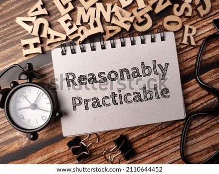 Clock,glasses,paper clips and notebook with text Reasonably Practicable on a wooden background.