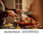 Cloe up of man carving roast turkey during Thanksgiving dinner in dining room. 