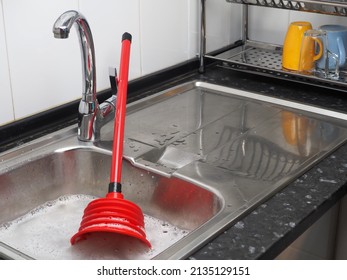 Clogged pipes in the kitchen. Sink full of dirty water, red plunger