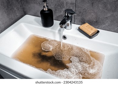Clogged sink in bathroom, sink with dirty water, brown soap. Plumbing problems.
