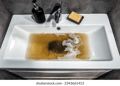 Clogged white sink in bathroom, sink with dirty water, brown soap. Plumbing problems.