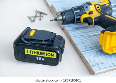 Close up 18 volt recharge Li-ion battery for electric cordless tool,saw,rotary hammer,drill,jigsaw,wrench on white.Blurred screwdriver,screws on gray-painted boards behind.Selective focus, copy space - Shutterstock ID 1989180101