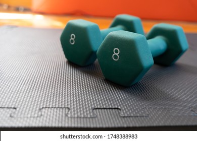 Close Up Of 2 Green Hexagonal, 8 Pound Dumbells Laying On Top Of A Black Gym Mat. 