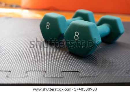 Close up of 2 green hexagonal, 8 pound dumbells laying on top of a black gym mat. 