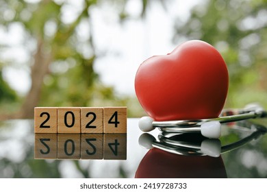 close up 2024 wooden text block, red heart and stethoscope on table, world health day, medical and healthcare, cardiology and cancer crisis risk and problem concept