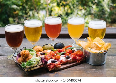 Close Up Of 5 Different Beer Glass  With Mix Finger Food On A Wood Table And Plants Background, Outdoor Natural Light, Aperitif, Happy Hour 