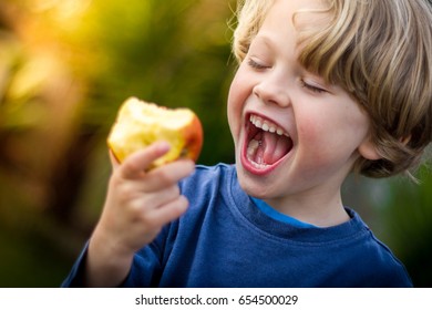 Close Up Of 5 Year Old Blonde Child With Mouth Open About To Take A Bite Of An Apple