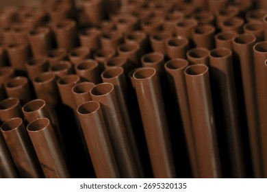 Close up abstract background of many brown hollow plastic straws. This large group creates uniform, repeating pattern with warm, organized feeling from top view