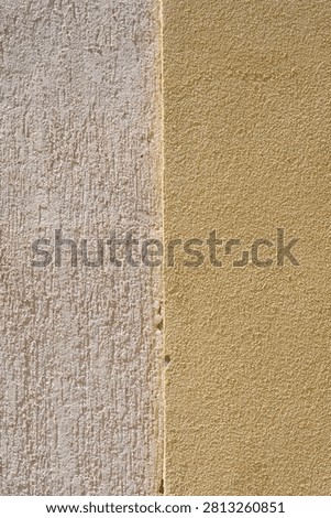 Close up abstract texture background of a two-tone plaster facade split vertically into a white grooved surface and a smooth yellow concrete finish