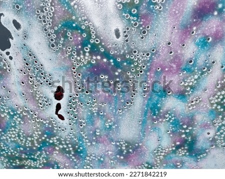 Close up abstract texture view of a car windshield in an automatic car wash, with colorful soap and water droplet designs